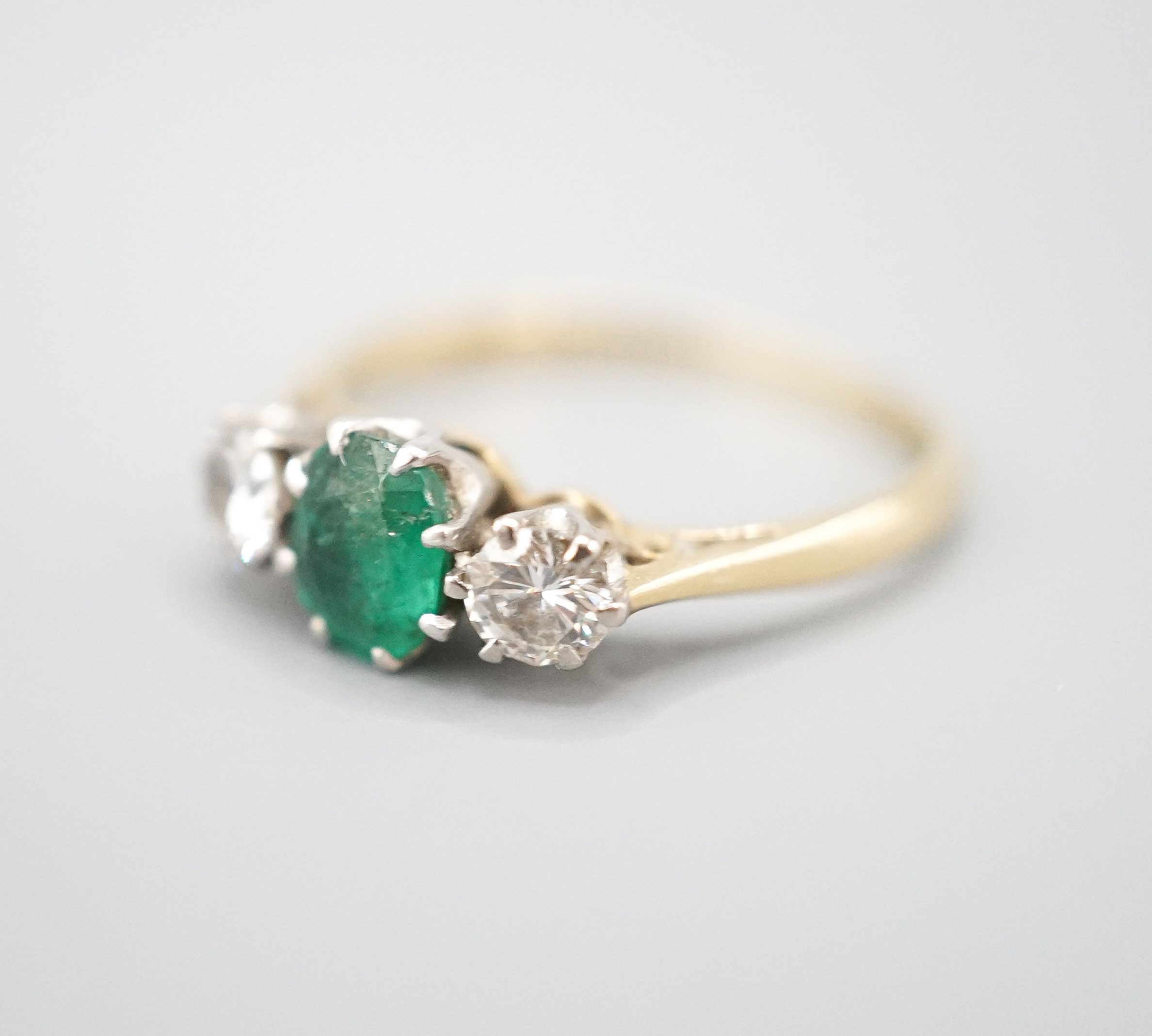 An 18ct and plat, emerald and diamond set three stone ring, size K, gross weight 2.3 grams.